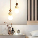 Luminária pendente LED estilo Bauhaus em acabamento creme com detalhes em pedra e madeira instalada sobre uma mesa de cabeceira em um quarto moderno.